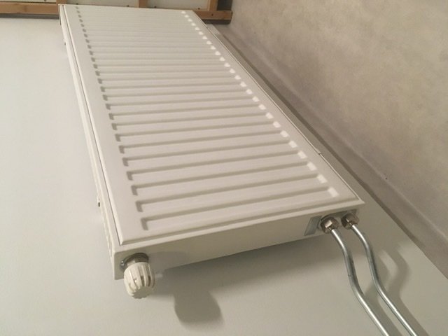 Vit radiator monterad på vägg med synliga rör och termostatventil.