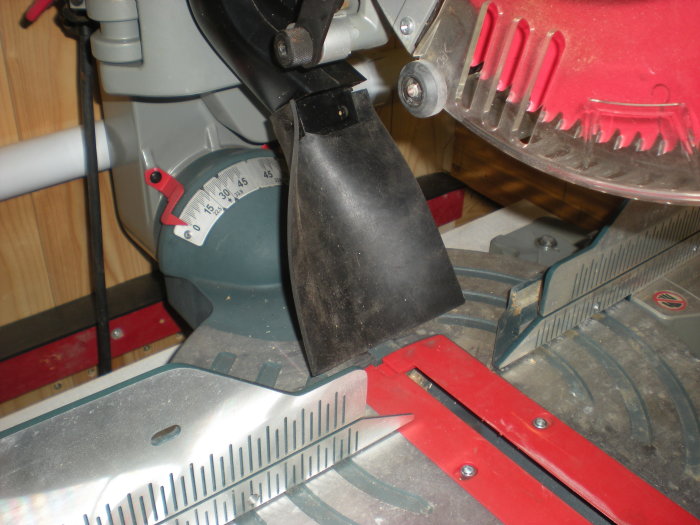 Förbättrad spånutsugsdel installerad bakom röd cirkelsågs klinga, sträcker sig ner mot sågbordet.
