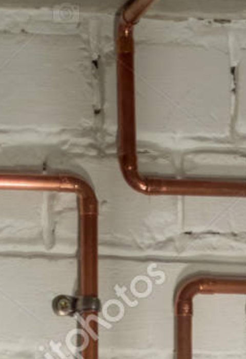 Kopparledningar lödda längs en vit vägg, illustrerar VVS-arbete och rörinstallation.