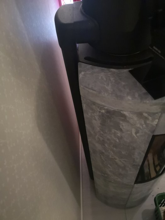 Svart plasthink i hörn med tapetserad vägg, delvis skymd syn.