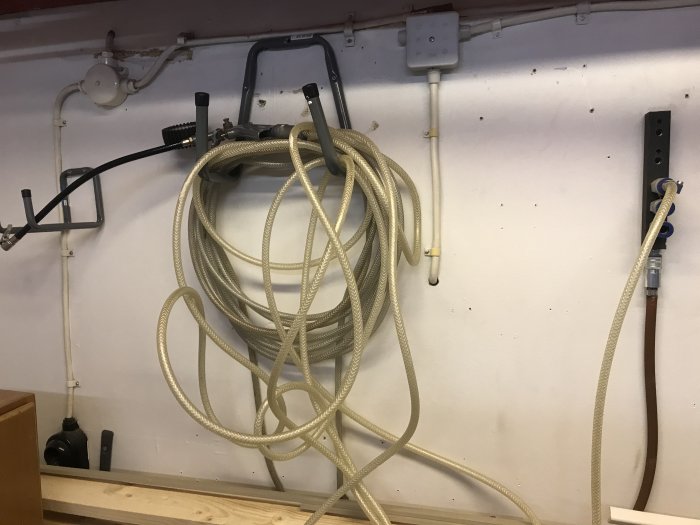 En upphängd kompressorslang som är cirka 5 meter lång, monterad på en vägg i ett verkstadsutrymme.