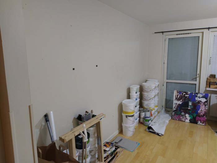 En ateljé med vita väggar och blandade konstmaterial inklusive hinkar och en målarduk.