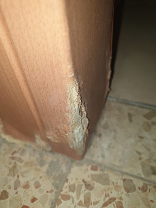Rikkinäisen oven reuna, josta näkyy esiin työntyvä valkoinen materiaali. Kuva liittyy huoleen mahdollisesta asbestista ovessa.