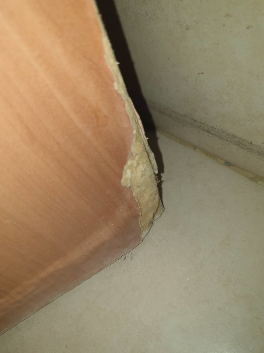 Oven alareuna, josta pilkistää vaalea materiaali, joka epäilyttää asbestina. Oven puupinta ja repaleinen kohta näkyvät selvästi.