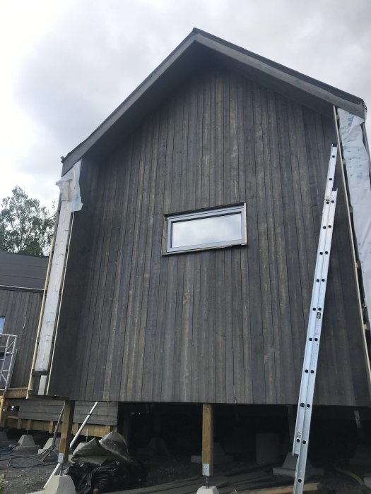 Träfasad målad med tjärvitriol, jämnt grå yta på ett 1 1/2 år gammalt hus med stegar.