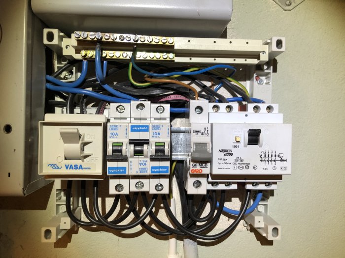 Öppet elskåp med säkringar och kopplade kablar, bland annat en strömbrytare märkt "VASAnorm" och säkringsautomater.