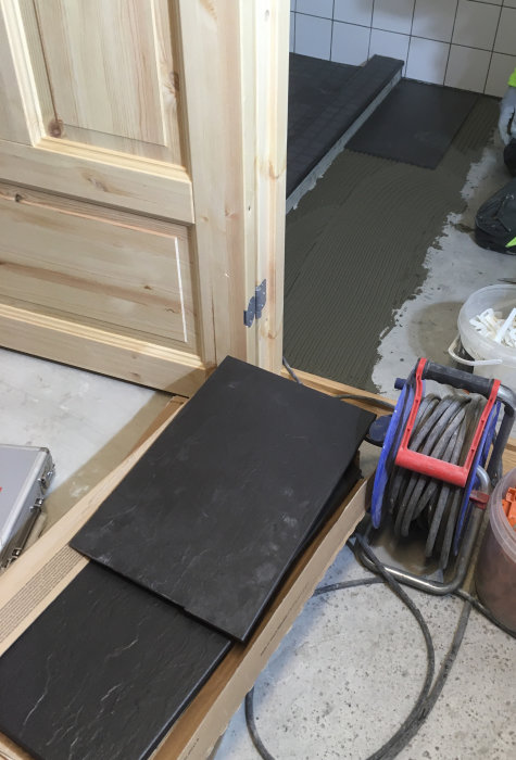 Installation av svarta kakelplattor på badrumsgolv med synlig kakelsättare och verktyg.