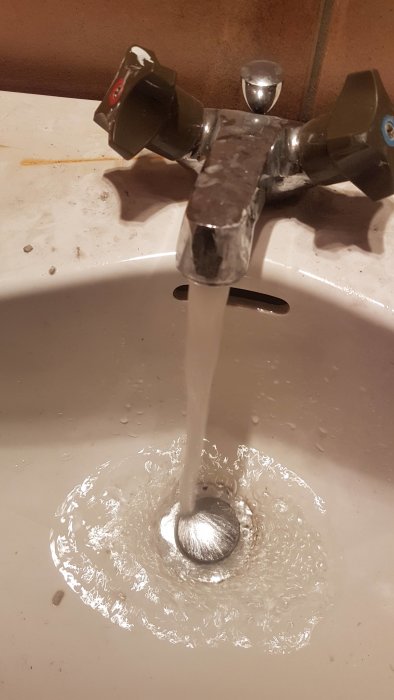 Vatten som rinner från en tvättställsblandare in i en handfatstropp.