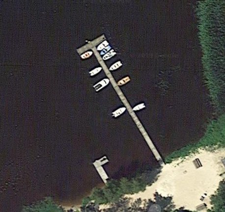 Satellitbild av en gemensam brygga med båtar i en sjö, med grillplats och båtbod på stranden.