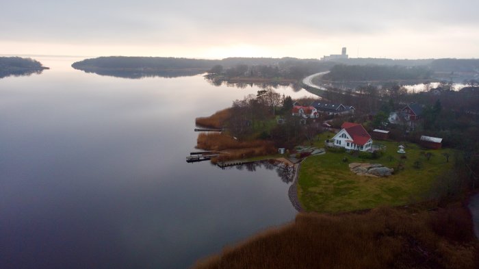 Vy över lugnt vattenlandskap med hus och bryggor tagen från en drönare vid skymningen.