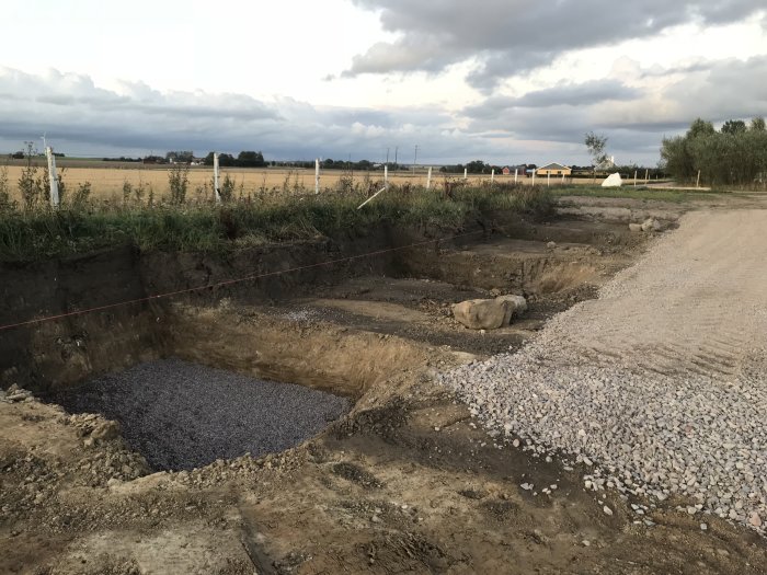 Grundarbetsplats för ridhus med förberedd plintgrop fylld med makadam och hårdgjord yta med grus.