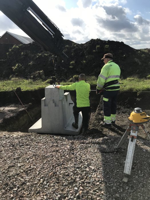 Arbetare positionerar en betongplint i grop med krantjänst vid grundläggning för ridhus.