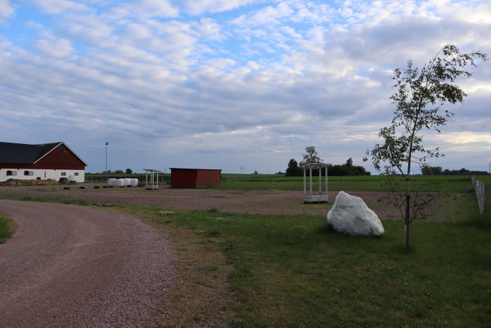 Ett tomt landskapsområde med avlägsna byggnader och marker förberedda för konstruktion, täckt med grus och delvis gräsmatta.