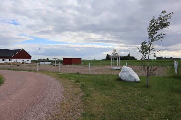 Jordbearbetad yta för byggnation med vita markeringsstolpar och en röd byggnad i bakgrunden på en bondgård.