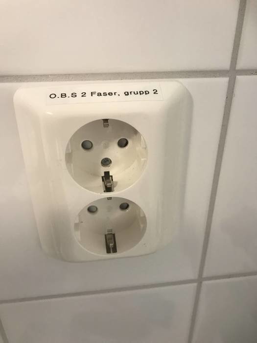 Infällt dubbeluttag på vit kakelvägg med texten "O.B.S. 2 Faser, grupp 2".