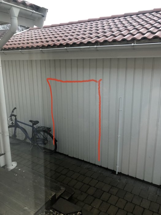 Garagevägg med markerat område i orange för planerad ytterdörr, cykel parkerad vid sidan.