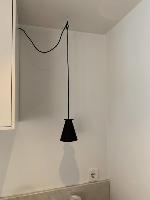 Köksutrymme för hyllplan mellan väggskåp och vägg, med nedhängande lampa och eluttag.