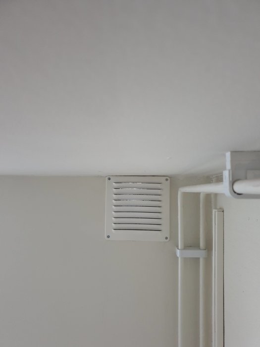 Vit ventilationsgaller på vägg ovanför ett vitt rör, kondensproblem i radhus diskuteras.