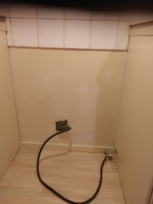 Hörn av ett kök med en tom vägg där en gammal spiskabel är urkopplad från vägguttaget.