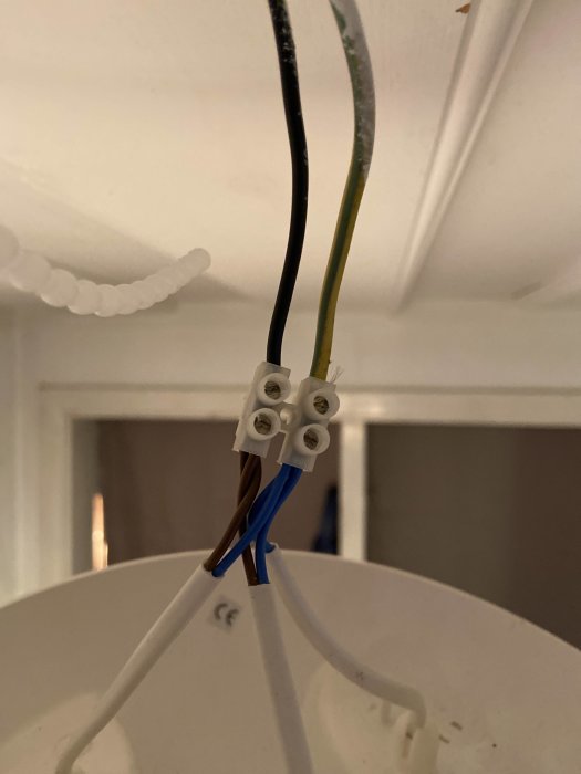 Takinstallation med en svart och gulgrön kabel ur taket kopplade till en brun och blå kabel på takarmatur.