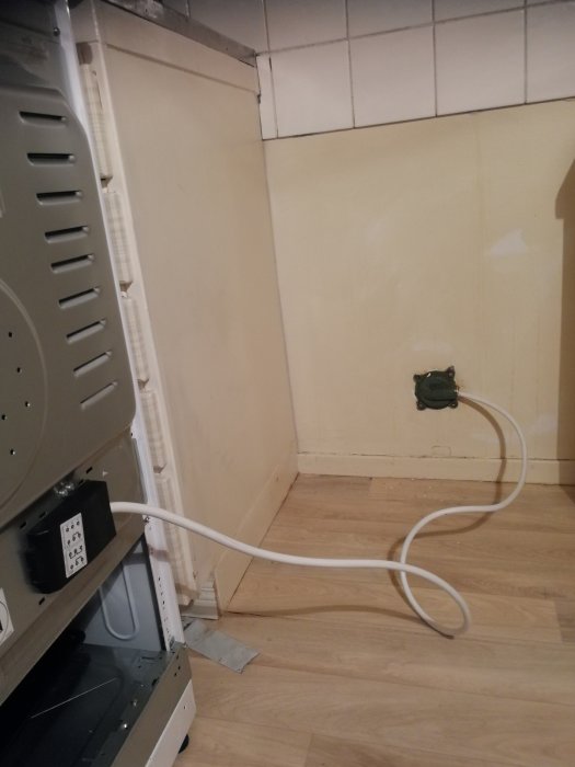 En nyligen installerad diskmaskin med anslutningsslangar, placerad vid en vägg med kakel och tapet.