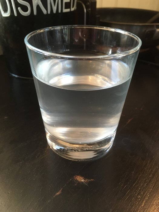 Glas med grumligt vatten på ett köksbord, med diskmedelsflaska i bakgrunden.