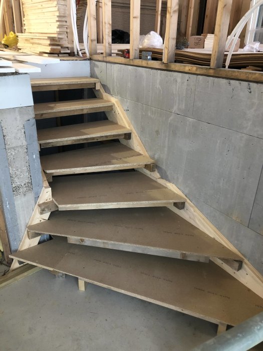 Outbyggd trätrappa med öppna steg som en mall för senare arbeten, i en byggmiljö med betong och trämaterial.