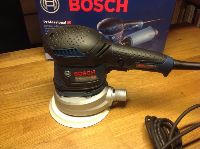 Bosch GEX 125-150 AVE excenterslipmaskin på bord med sladd och förpackning i bakgrunden.