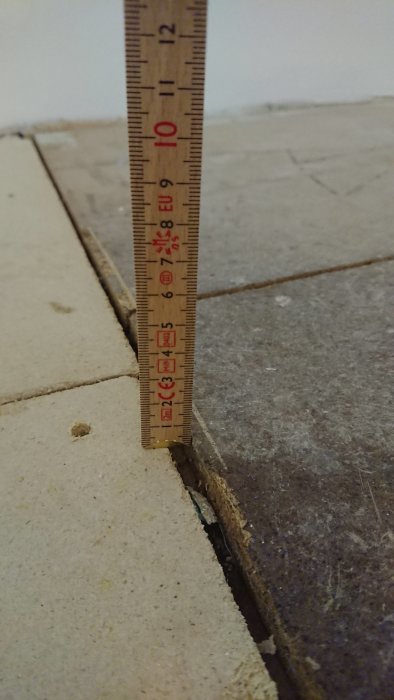 Måttstock visar en nivåskillnad på ungefär 4-5 mm mellan golvspånskivor i renoveringsprojekt.