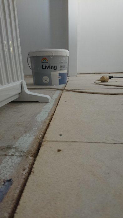 Nivåskillnad mellan två golvspånskivor i ett renoveringsprojekt, med en målarhink och borrsladd i bakgrunden.