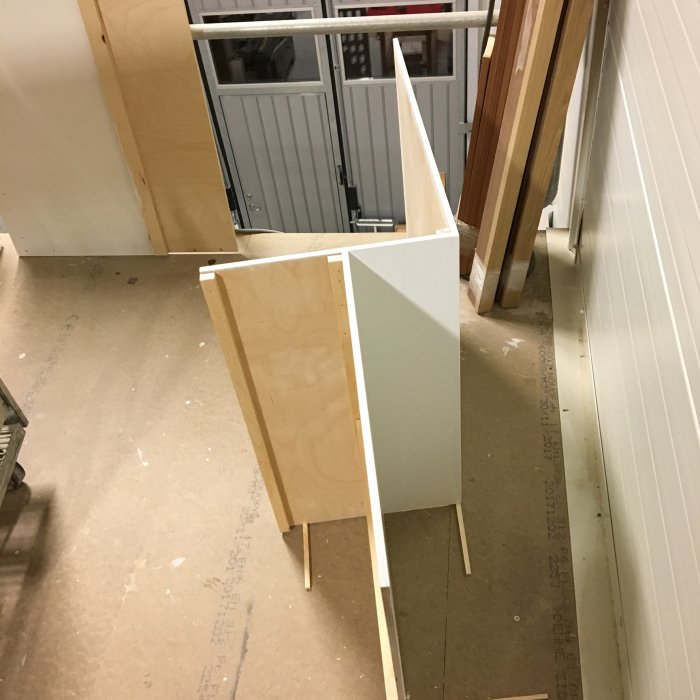 Delar av ett nytt underrede till möbler i plywood står i en verkstad, målade i grå och vit.