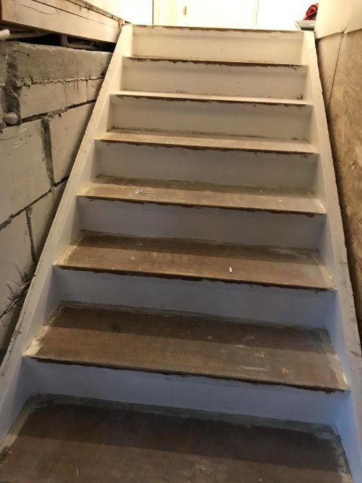 Trappa med ojämna steg och synliga vagnsstycken mot en betongvägg, i behov av renovering.