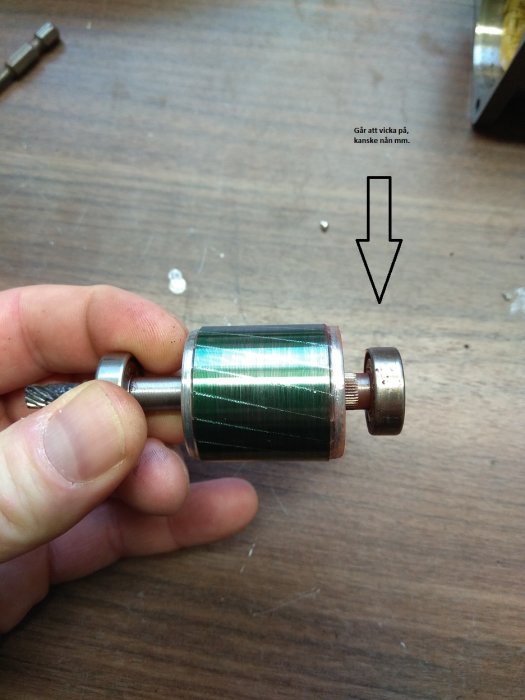 Hand håller isärplockad motoraxel med notering om att det går att vicka på delen.