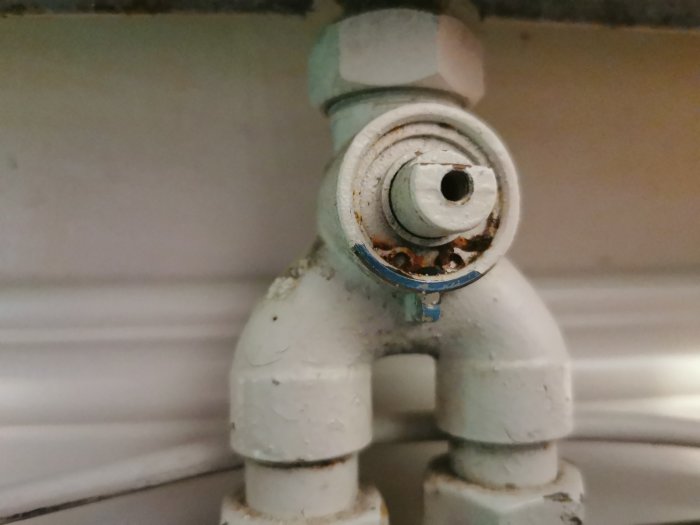 Närbild på gammal vitmålad termostatventil på en radiator, med rost och avflagningar.
