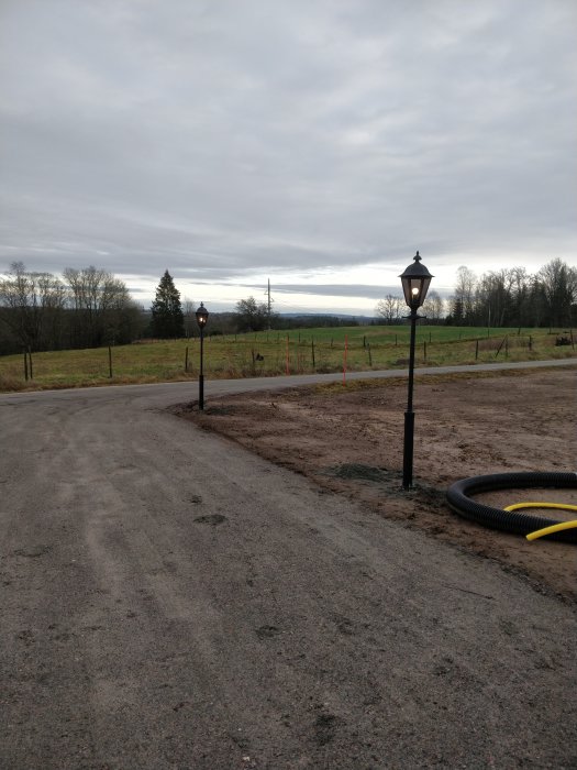 Två lyktstolpar installerade längs en grusväg med öppet landskap i bakgrunden.