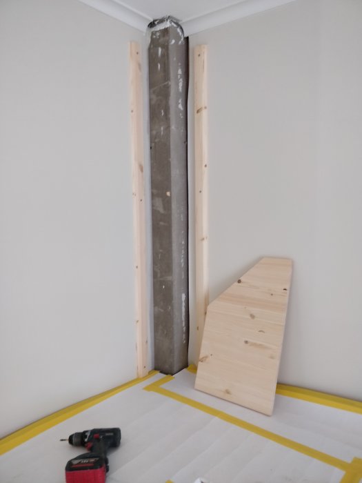 Gipsad pelare med reglar i ett rum under renovering, verktyg och virkesbit på golv med skyddsplast.