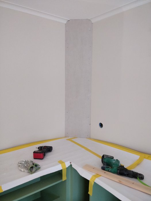 Gipsad pelare med skyddsplast på golvet, verktyg och trämaterial under renovering.