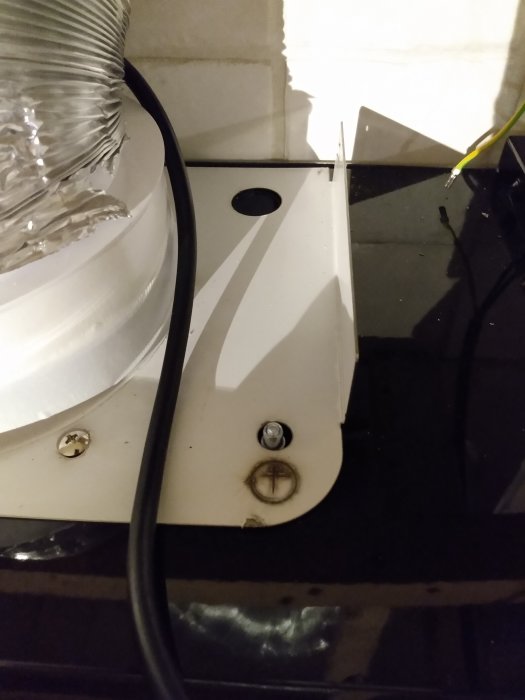 Vit kåpa med jordad nit och svart jordkabel nära ventilationsrör och reflekterande yta.