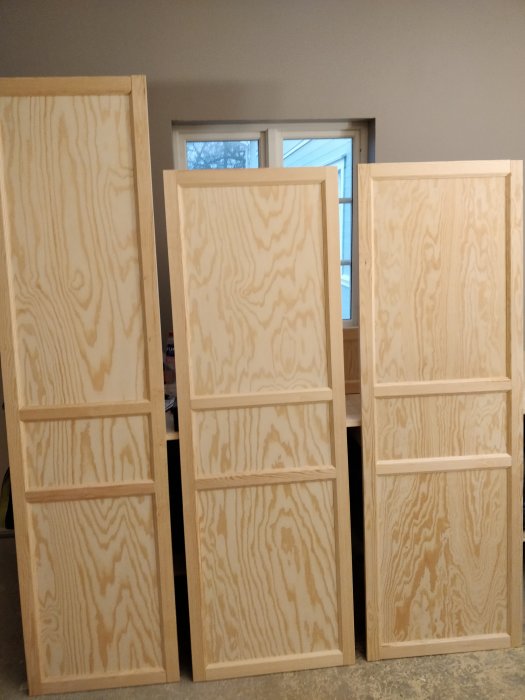 Hemsnickrade köksluckor i furuplywood med planhyvlade ramar, stående i ett rum.