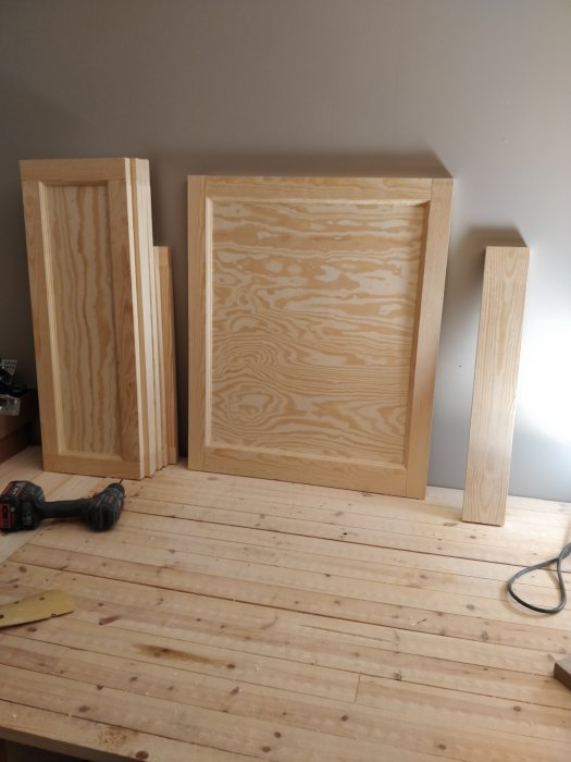 Hemsnickrade köksluckor i olika storlekar av furuplywood och ramverk, placerade på ett trägolv.
