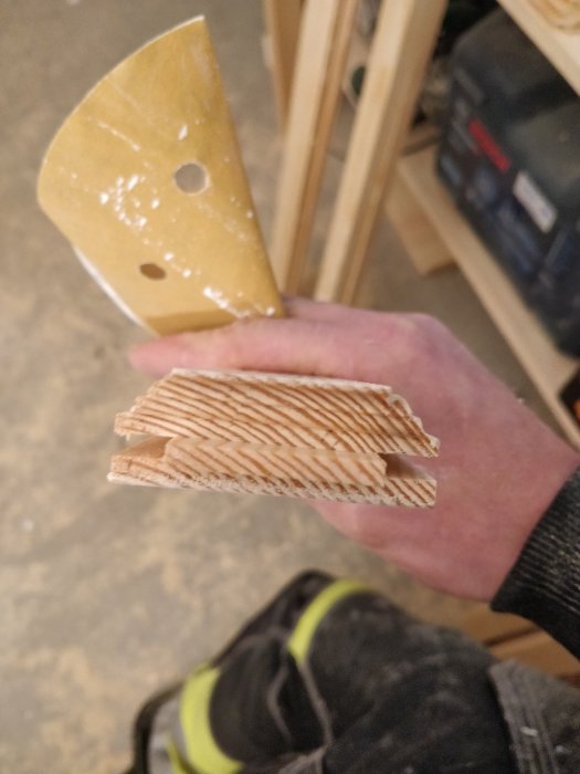 Hand håller träbit med fräst profil för köksluckor i en snickeriverkstad.