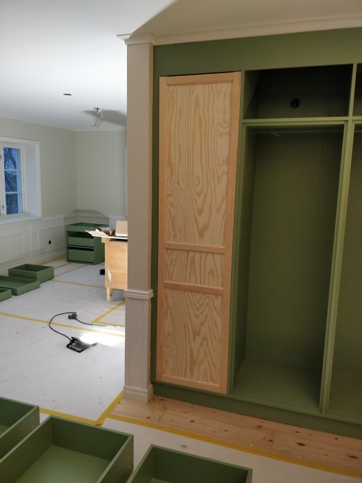Hemsnickrade köksluckor av trä monterade i en enda hög skåpstomme, i ett rum under renovering.