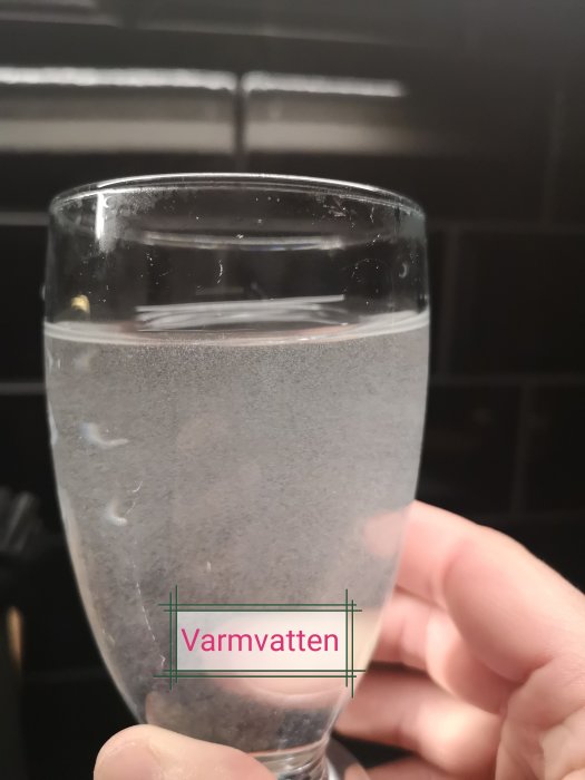 Ett glas med varmvatten som innehåller synliga småpartiklar och textetiketten "Varmvatten".