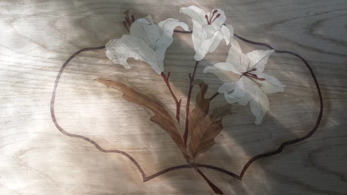 Intarsia-arbete med blommotiv i trä på slipat träunderlag.
