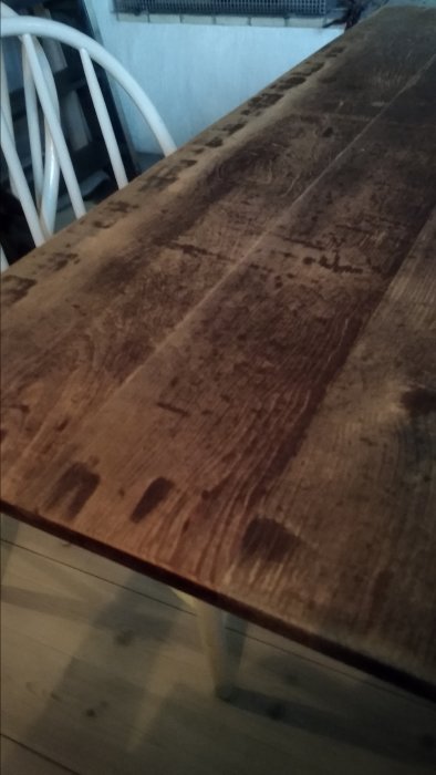Nötta ytor på ett gammalt matbords iläggsskiva av fanér med synliga tecken på slitage och användning.