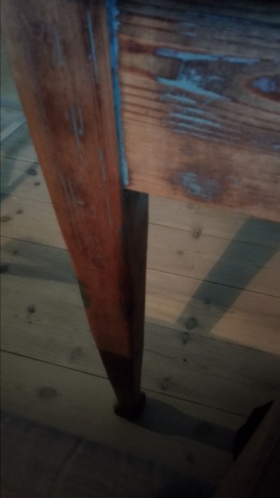 Närbild på benet av ett gammalt trämatbord med synliga slitage och skador, med fokus på träets textur och färgnyanser.