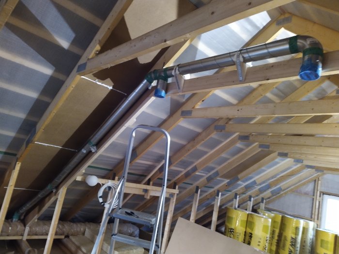 Ventilationsrör installerade i taket på en vind med synliga takbjälkar och isoleringsmaterial.