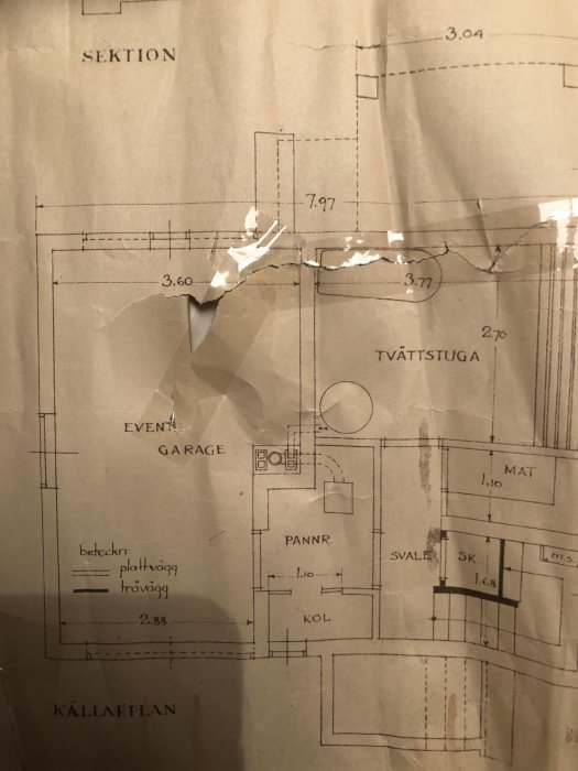 Skadad och delvis sönderriven ritning av källarplan med markerade rum som garage, tvättstuga och pannrum.