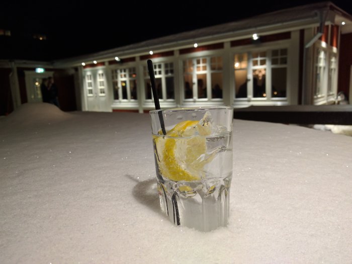 Drinkglas med citron och is på ett snöbeklätt bord utomhus med en byggnad i bakgrunden under kvällstid.