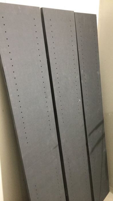 Förberedda träskivor för möbelbygge med många borrade hål stående mot en vägg.